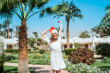 Summer portrait of beautiful happy girl in santa claus costume, tropical palm trees on the beach by the ocean, sea holidays, christmas at sea. summer vacation concept, travel.