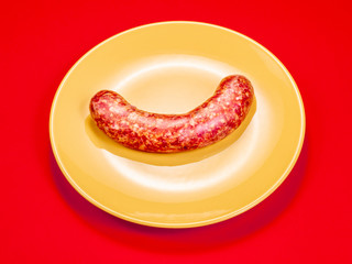 raw chorizo sausage in yellow plate on red background