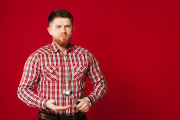 Angry bearded worker in a shirt standing with his socket wrench on red background.