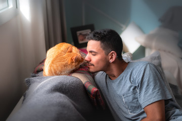 primer plano de hombre joven y gato atigrado acercandose con cariño