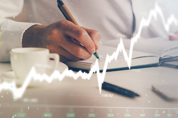 Double exposure of man's hands writing notes of stock market with forex chart.