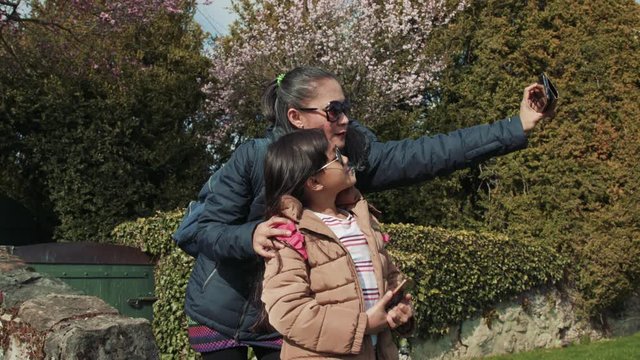 An asian mother and her daughter shoot a selfie in front of trees and flowers