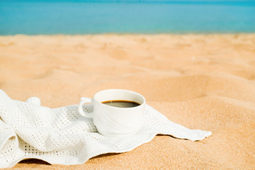 coffee espresso cup with ocean , beach and seascape. Blue sky, white sand, woven zonik, wooden beach chair. Sea vacations. The concept of travel, rest and relaxation.