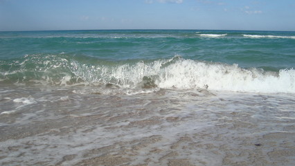The Sea green wave runs over the smooth sandy beach, leaving a white foam on the sand.
