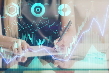A woman hands writing information about stock market in notepad. Forex chart holograms in front. Concept of research.