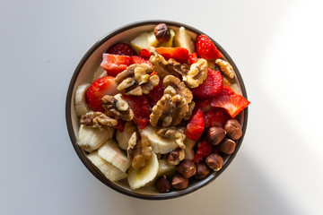 Healthy breakfast. Fresh porridge, with strawberry, banana and nuts in a bowl on white background. Top view.