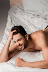 Fototapeta na wymiar sexy smiling man in jeans lying on bed on grey