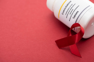red awareness aids ribbon and container with emtricitabine tablets on red background