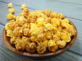 High angle view of delicious popcorn in round wooden plate isolated on blue wooden background. Include buttery caramel corn and rich cheddar cheese corn. Food and snack concept. With copy space.
