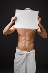 sexy shirtless man in towel holding blank placard in front of face isolated on black