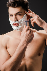 sexy nude bearded man shaving face with razor isolated on black