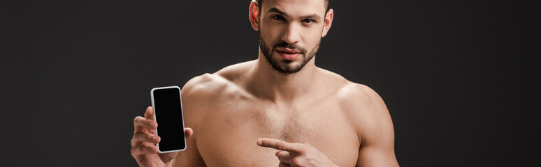 Fototapeta premium panoramic shot of sexy nude man pointing at smartphone with blank screen isolated on black