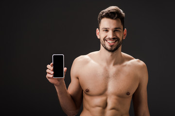 Fototapeta premium smiling sexy naked man showing smartphone with blank screen isolated on black