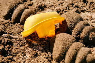 Used yellow toy boat lying upside down between sand shells on the sandy ground in the sun. Seen in Germany in March.