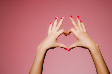 Frauenhände mit heller Maniküre isoliert auf rosafarbenem Hintergrund Liebeszeichen mit den Fingern nach oben