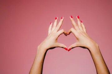 Photo sur Aluminium ManIcure Mains de femme avec manucure lumineuse isolées sur fond rose signe d& 39 amour doigts vers le haut