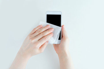 Girl hands rubs white smartphone with a disinfectant wipe.