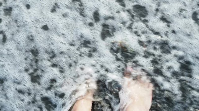 A sea wave is washing bare feet. Summer freshness of the sea wave. Male legs covered by a wave. The sea wave washes the sand off your feet.
