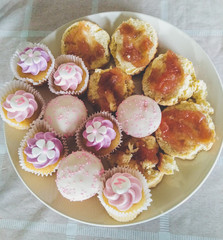 pink frosted cupcakes and jam scones on a plate