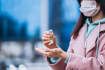 Close up hands of female in medical mask cleaning her hands with sanitizer outdoor in the city to prevent virus deseases. Coronavirus, COVID-19, epidemic, pandemic, quarantine concept.