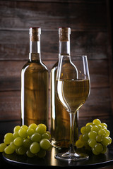 Two white wine bottles with a glass and grapes on a wooden background