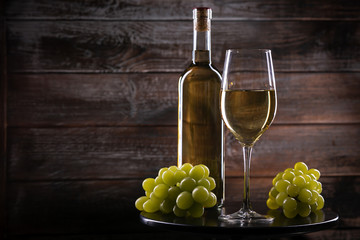 Wite wine bottle and a full glass and grapes on a table on a wooden background