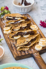 French delicious ruddy crepes - thin fried sweet pancakes stuffed with chocolate hazelnut paste, bananas. Folded crepes, pancakes on wooden board.