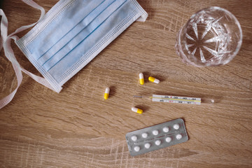Pills, thermometer and a glass of water on the wooden table.
