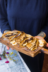 Woman holds delicious french chocolate crepes - thin fried sweet folded pancakes stuffed with bananas and paste. Homemade. Wooden board