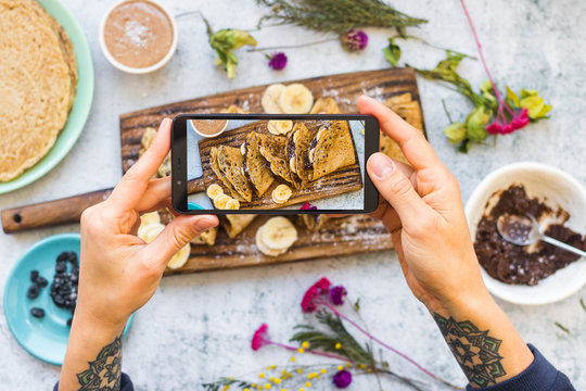 Woman hands make photo of french crepes - thin fried sweet pancakes with phone. Smartphone food photography picture.
