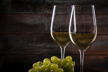 Two full white wine glasses with grapes on a table on a wooden background