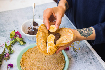 French crepes - thin fried sweet pancakes. Woman makes stuffed crepes with bananas and chocolate paste.