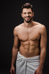 Fototapeta na wymiar smiling sexy muscular man in towel isolated on black