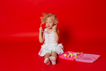 Adorable smiling little girl playing at the doctor listening toy stethoscope isolated on red