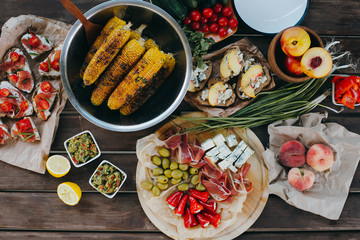 Summer picnic or BBQ food concept. Selection of vegetables, sandwiches, grilled corn and meat. Top view table scene on a wood background.