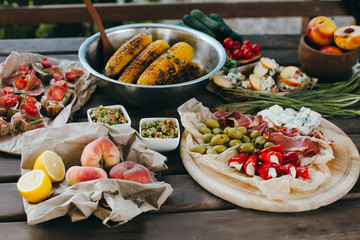 Summer picnic or BBQ food concept. Selection of vegetables, sandwiches, grilled corn and meat. Top view table scene on a wood background.