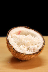 Coconuts with coconut flakes are isolated on a wooden table on a black background