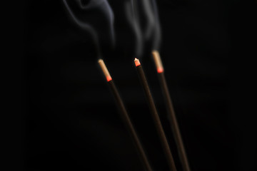 Close up of burning incense sticks with smoke over black background
