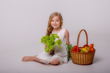 a blonde girl with a basket of fresh vegetables smiles on a gray background, a healthy food concept for children