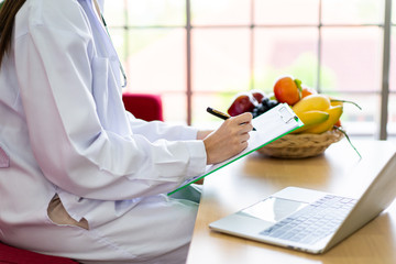 Happy Asian nutritionist working in her office in hospital. Specialist in nutrition chatting to a patient by using laptop computer in the office. Professional nutrition consultant portrait.
