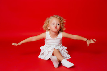 Beautiful little curly blonde girl makes kissing face on the floor isolated on red