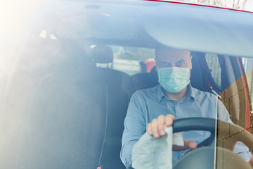 Autofahrer mit Mundschutz desinfiziert Lenkrad