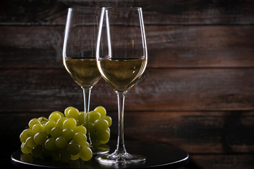 Two full white wine glasses with grapes on a table on a wooden background