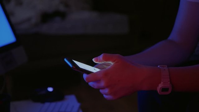 Moody and atmospheric video of young woman hold smartphone in dark room with neon fluoroscent lights. Addicted to internet and social media attention. Keep in touch with friends