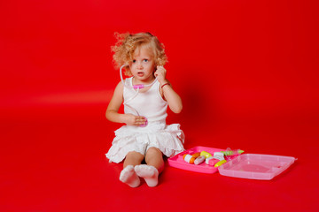 Adorable smiling little girl playing at the doctor listening toy stethoscope isolated on red