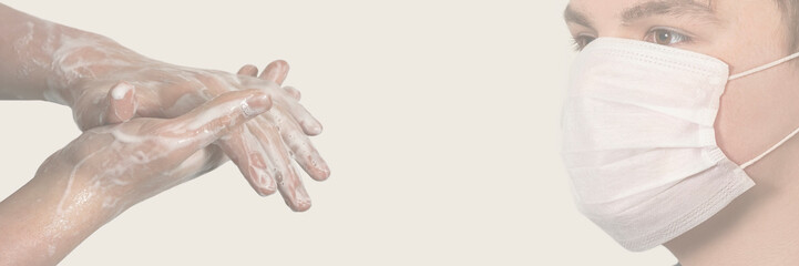 Fototapeta premium Corona virus. Young guy in a medical protective mask and washing his hands with soap on a gray background. Protection against viruses, infections.