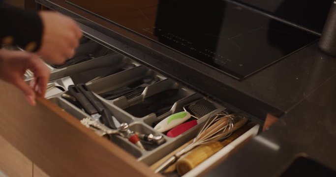 Woman opens a kitchen cabinet that is filled with various cooking and eating tools, takes a couple of items and the closes the cabinet. Cabinet is being gently automatically closed by itself.