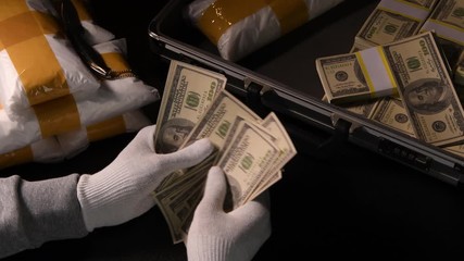 Hands counting money with packs of narcotic drugs and money in the background .