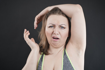 Fototapeta premium unhappy woman shows her unshaved armpit. plus size middle age woman is not happy with hair in her armpits. Caucasian girl is emotional sad and upset. black background in the photo Studio.