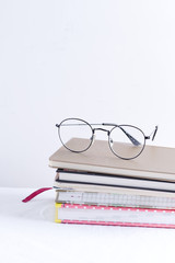 Stack of note books for notes and annotations with glasses on the top on a white table.